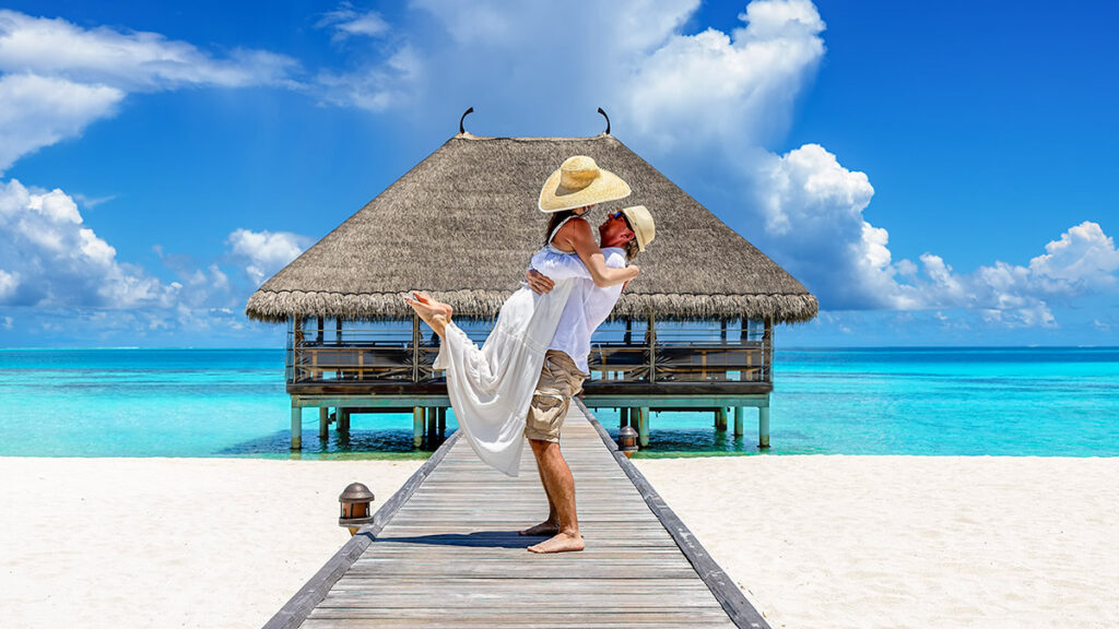 A happy couple in white summer clothing hugging on a wooden pier